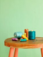 Colorful spools of thread on a vintage stool in front of a green wall