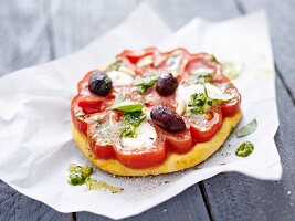 Mini pizza topped with beef tomato, olives and pesto