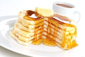 Gestapelte grosse Pancakes mit Butter, Ahornsirup und einer Tasse Kaffee