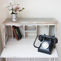 Aufgeklappter weisser Sekretär mit altem Telefon, Büchern & Blumen