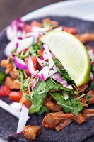 A taco with jackfruit, lettuce, radishes, coriander and lime