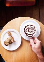 Hand hält eine Tasse heiße Schokolade, daneben ein Stück Bananen-Nuss-Muffin