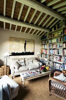 Gemütliches Wohnzimmer mit Sitzgruppe im Landhausstil und Bücherwand unter rustikaler Holzbalkendecke