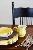 Yellow plates, bowls, milk jug and cutlery on a wooden table