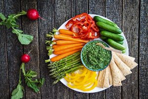 A plate of raw vegetables with a herb dip and crispbread