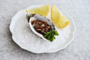 A fresh oyster with lemon wedges on rock salt