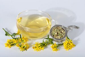 Goldenrod tea in a glass cup, dried tea leaves and fresh flowers
