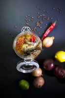 Pickled fried herring in a jar with lemons, limes, chilli peppers and onions