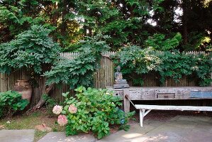 Blühende Büsche im Garten und rustikale Werkbank vor Holzzaun