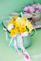 Yellow spring posy of tulips, carnations and narcissus in turquoise teapot