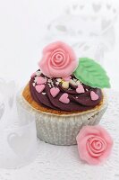 A cupcake decorated with chocolate cream and a marzipan rose for Valentine's Day