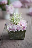 Arrangement of lily-of-the-valley and hydrangeas in small, vintage container