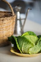 A savoy cabbage next to a straw basket and an olive oil jug