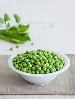 A bowl of fresh peas with pea pods in the background