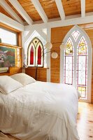 weiße Balken und Naturholz im Kontrast zu gotischen Formen und farbiger Bleiverglasung in künstlerisch inspiriertem Schlafzimmer in Taos (New Mexico)