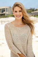 A young blonde woman on a beach wearing a beige knitted jumper