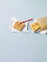 Two slices of tray bake cake on paper plates and in a paper bag