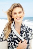 Junge, blonde Frau am Strand mit weiss-blau gemusterter Strickjacke mit Schalkragen