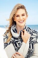 Junge, blonde Frau am Strand mit weiss-blau gemusterter Strickjacke mit Schalkragen