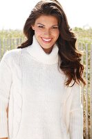 A young brunette woman outside wearing a white knitted roll-neck jumper