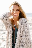 A young blonde woman by the sea wearing a beige knitted cardigan
