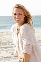 A young blonde woman by the sea wearing a white woollen jumper