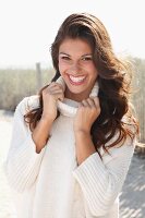 A young brunette woman outside wearing a white knitted roll-neck jumper