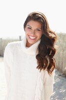 A young brunette woman outside wearing a white knitted roll-neck jumper