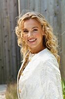 A young blonde woman outside wearing a white coat