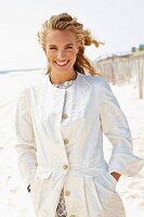 A young blonde woman on a beach wearing a white coat