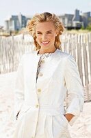 A young blonde woman on a beach wearing a white coat