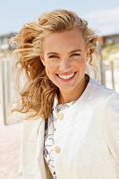 A young blonde woman on a beach wearing a white coat