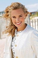 A young blonde woman on a beach wearing a white coat