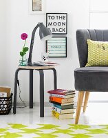 A black retro table lamp on a matching stool next to a stack of books on the floor and a partially visible armchair with a black leather cover