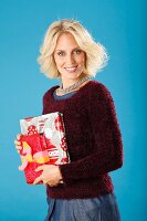 A young blonde woman holding presents and wearing a dark red jumper