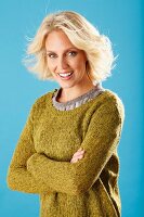 A young blonde woman with her arms folded wearing an olive-green knitted jumper