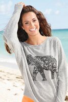 A young brunette woman by the sea wearing a grey sweatshirt with an elephant print