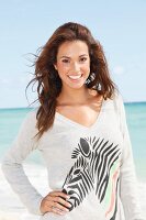 A young brunette woman by the sea wearing a grey, zebra-print jumper