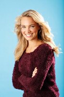 A young blonde woman with her arms folded wearing a burgundy knitted jumper
