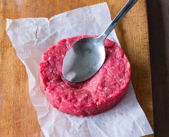 A raw hamburger being squashed with a spoon