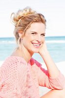 A blonde woman by the sea wearing a pink summer jumper