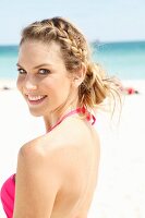 Junge, blonde Frau in pinkfarbenem Bikinioberteil am Strand