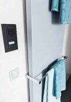 A flat panel radiator with a towel rail next to a built-in radio and lighting controls