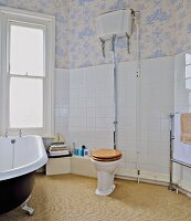 Toilet with vintage cistern, free-standing bathtub and toile-de-jouy wallpaper in bathroom with white wall tiles