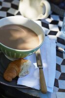 Café au Lait und Croissant zum auf Bistrotisch mit Rautenmosaik