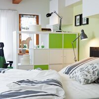 Blick vom Bett auf Raumteilerregal mit geschlossenen Elementen in weiss und freundlichem Grün; Retroanklänge bei Leuchten und Bettbezug