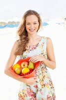 A young woman wearing a summer dress holding a hat filled with fruit