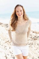 A happy young woman on the beach wearing shorts and crocheted jumper