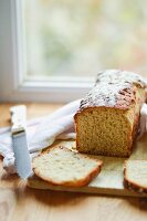 Bread and a knife on a wooden board in front of a kitchen window