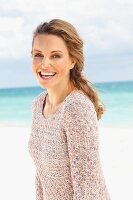 A blonde woman on a beach wearing a long, knitted jumper